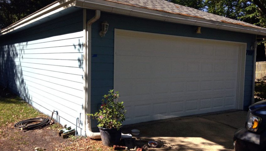 A white garage with blue trim and a tree in the corner.