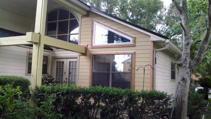 A house with trees in the background and bushes around it.