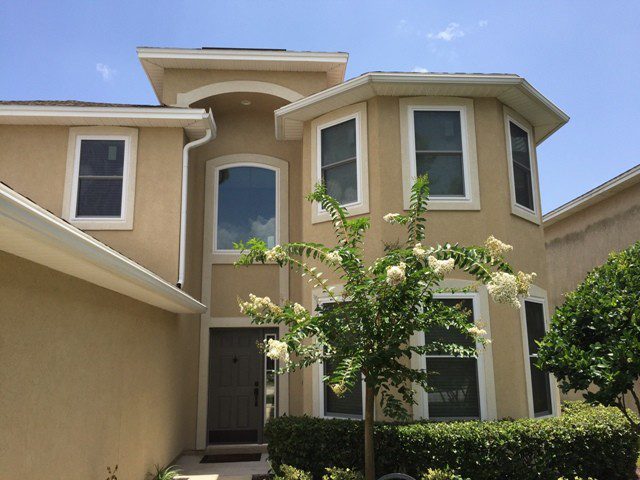 A large beige house with a tree in front of it.